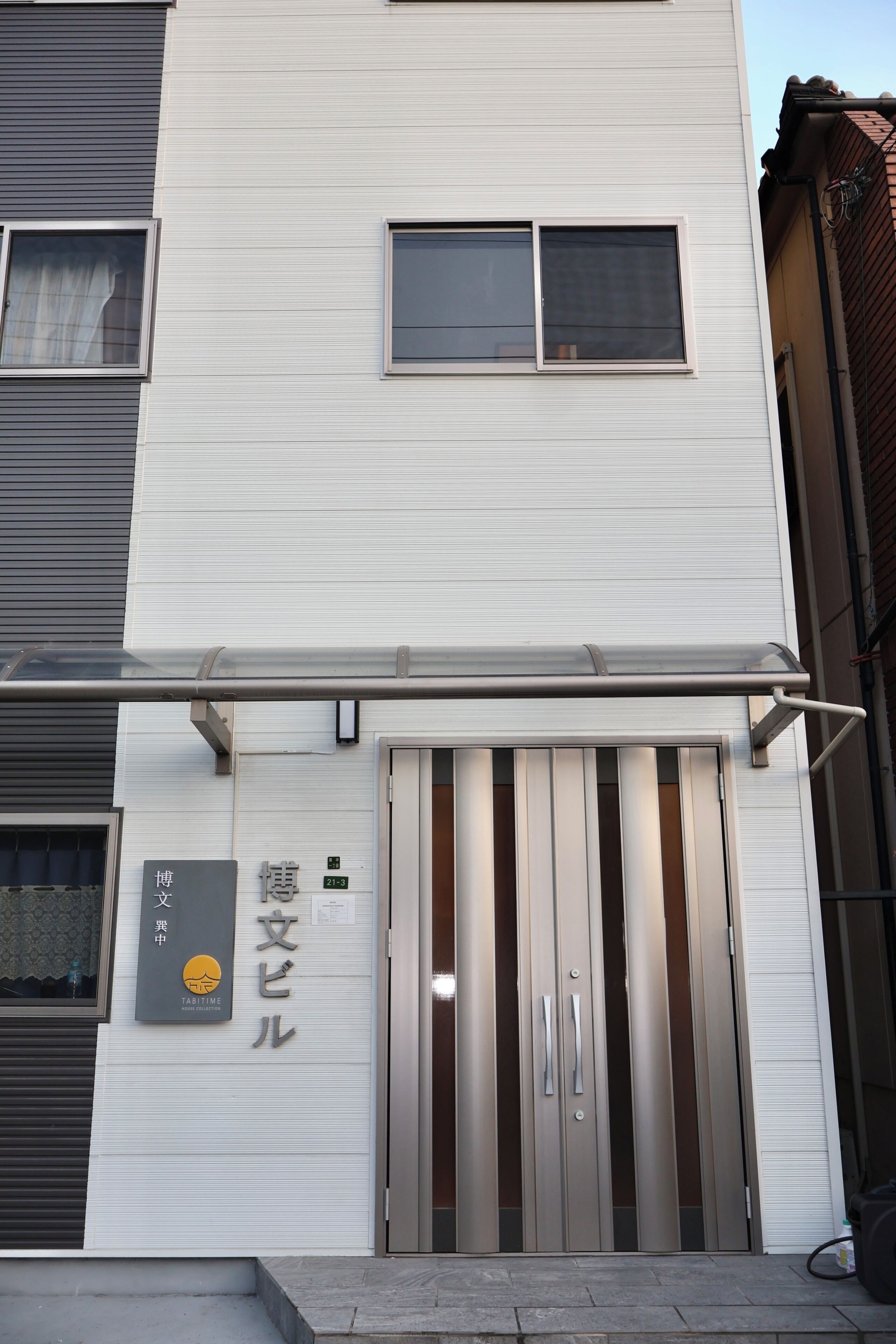 A modern building with a metal-framed entrance and a sign indicating a house collection.