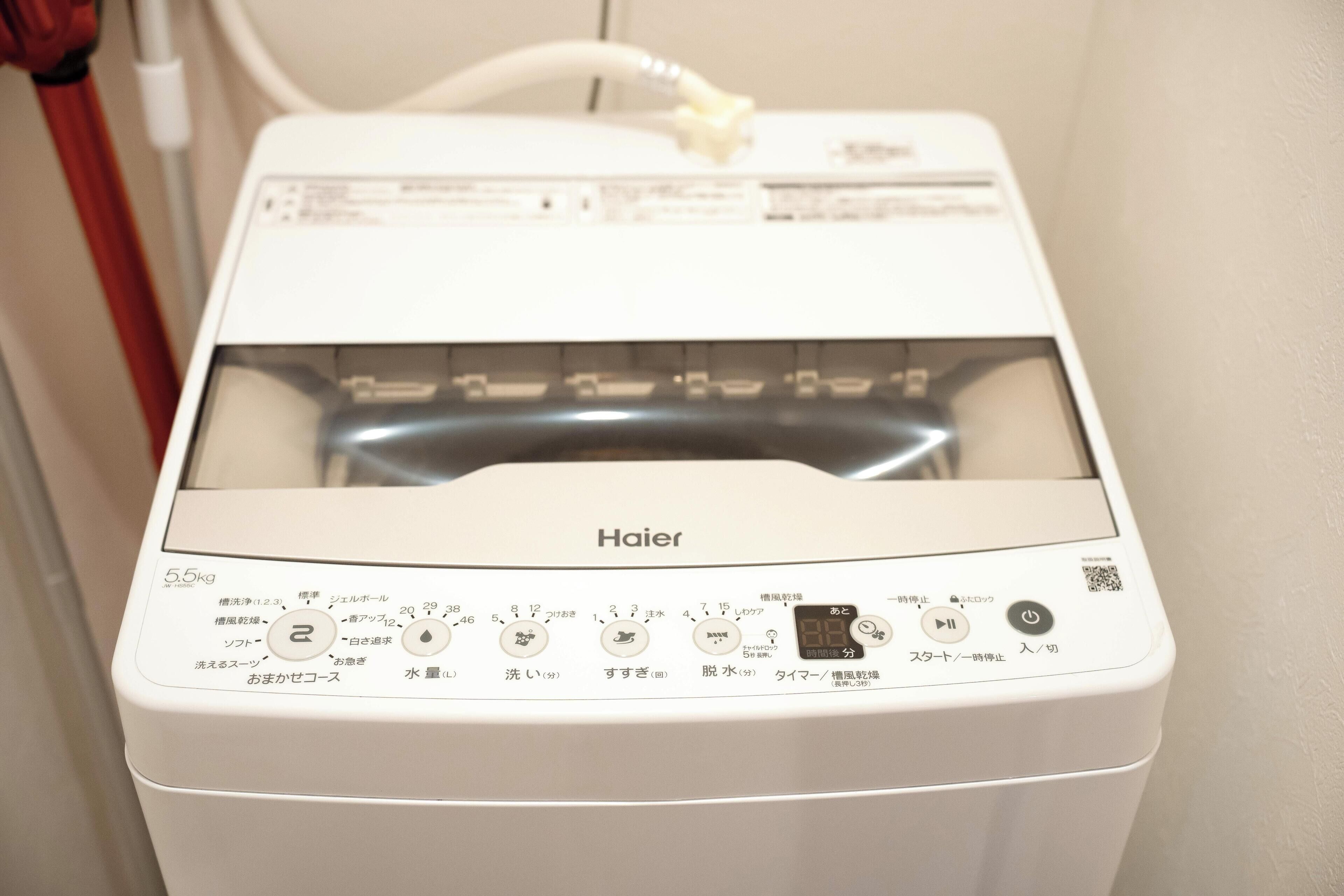 A white Haier washing machine with a transparent door, control panel with Japanese instructions, and a water inlet hose.