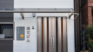 Un bâtiment doté d’une grande porte métallique, d’une enseigne avec des caractères japonais et d’une petite fenêtre ornée d’un rideau.
