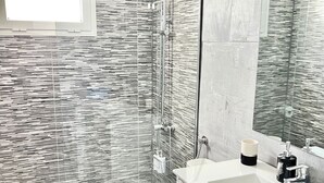A modern bathroom with a glass shower enclosure, a white vanity with a large mirror, and a textured wall design. - Sea and Beach (Puerto del Carmen)