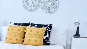 A neatly made bed with a yellow blanket and two mustard-colored pillows, a white nightstand with a lamp, and two decorative wall plates above the bed. - Sea and Beach (Puerto del Carmen)