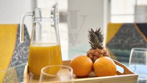 A breakfast tray with a pitcher of orange juice, two oranges, and a pineapple on a glass table with a view of the sky through large windows. - Sea and Beach (Puerto del Carmen)