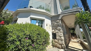 Une maison moderne avec une façade en pierre, de grandes fenêtres et un balcon agrémenté de plantes.