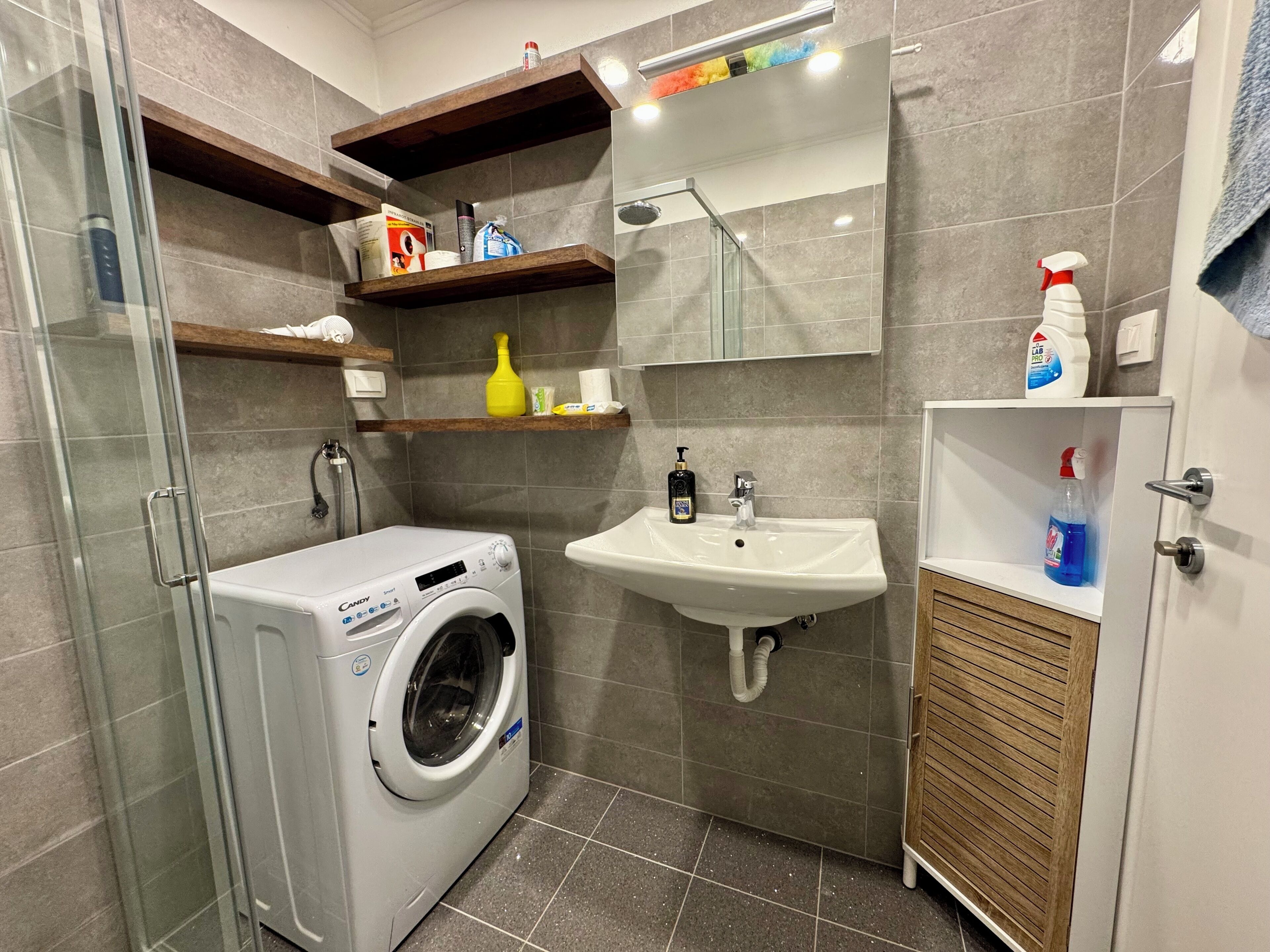 A compact bathroom with a washing machine, a sink, and a mirror.