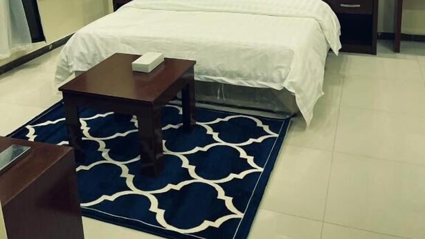 Una moderna camera d'hotel con un grande letto, un comodino e un tappeto blu con motivo.