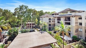 Un hotel de varios pisos con terraza en la azotea, rodeado de palmeras y una piscina.