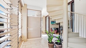 Un pasillo con una escalera, plantas en macetas y vista a una playa a través de una ventana.
