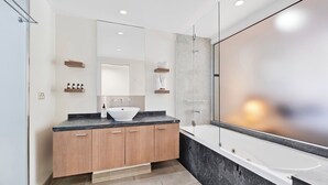 Une salle de bain moderne avec un grand miroir, une baignoire sur pieds et un meuble-lavabo en bois doté d’un vasque blanche.