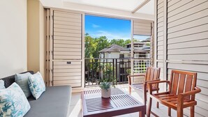 Un balcon avec un canapé, deux chaises en bois, une table et un pot de fleurs.