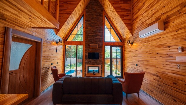 A cozy interior with a wooden ceiling, a fireplace, and a view of the outdoors through large windows. - SAPANCA GRANDWOODEN SUİT  (Sapanca)