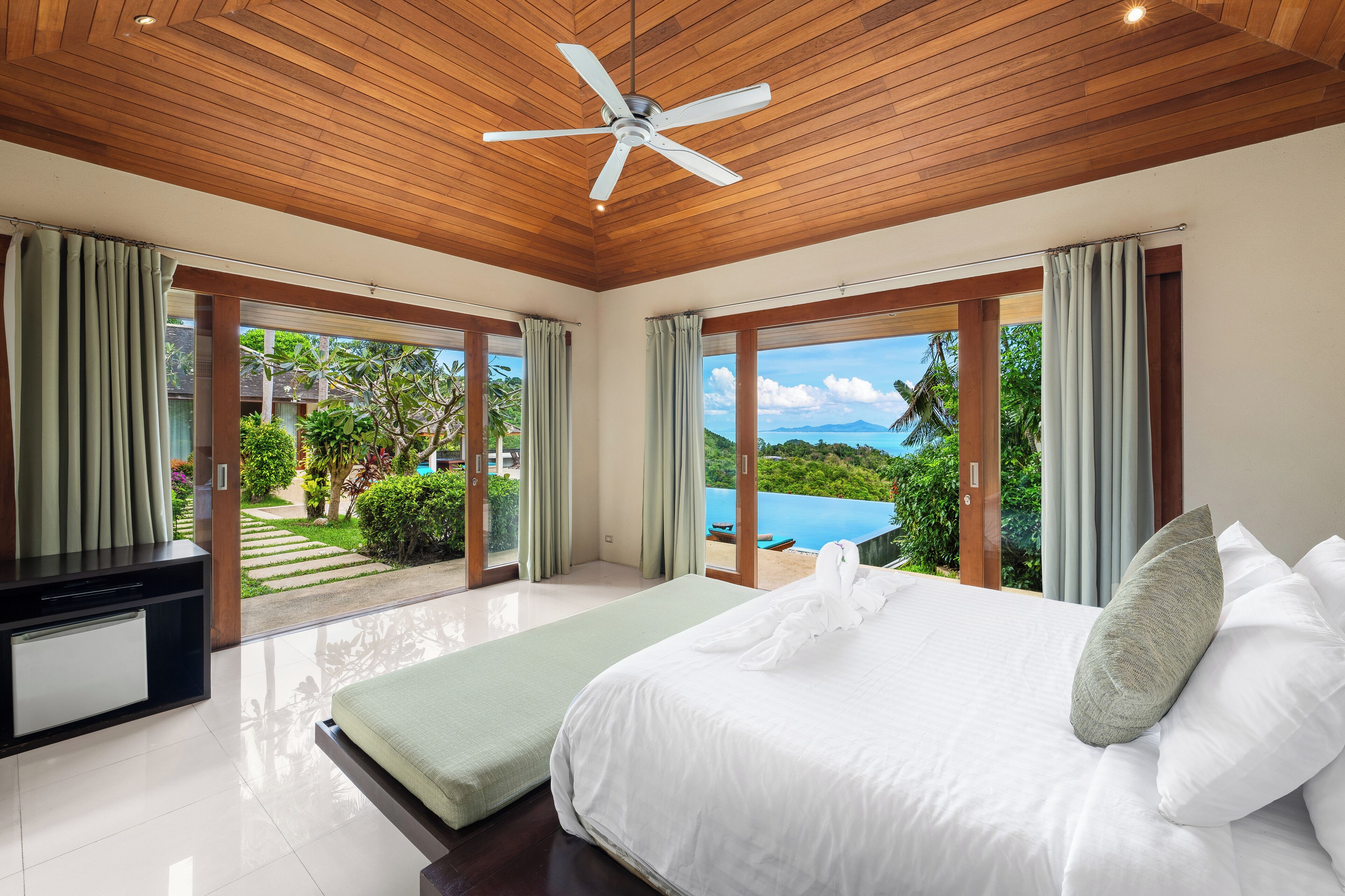 Un dormitorio con cama, televisor y vistas a una piscina y follaje.
