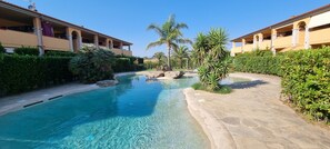 A pool area with clear water, surrounded by stone pathways and lush greenery.
