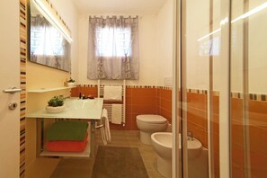 A bathroom with a glass shower enclosure, a white sink with a mirror above it, a toilet, and a bidet.