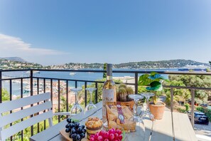 Un balcon avec une table dressée pour un repas, donnant sur une marina et des collines.