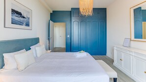 A bedroom with a large bed, a white headboard, a blue wardrobe, and a hanging light fixture. - BELLE DARSE AP4454 By Riviera Holiday Homes (Villefranche-sur-Mer)