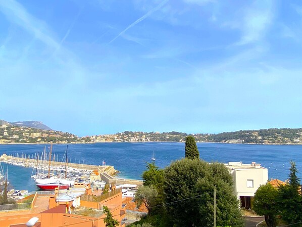 Un port de plaisance avec des bateaux, un ciel bleu azur et une ville côtière en arrière-plan.