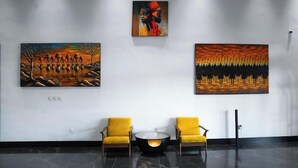 Eine Lobby mit zwei gelben Sesseln, einem runden Tisch und drei Kunstwerken an der Wand.