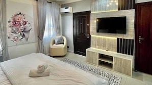 Ein modernes Schlafzimmer mit einem großen Bett, einem an der Wand montierten Fernseher, einem Sessel und einer Wanddekoration.