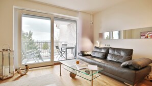 A modern living room with a glass coffee table, a leather sofa, and a sliding glass door leading to an outdoor patio. - Strandschlösschen Apartment 27 (Haffkrug)