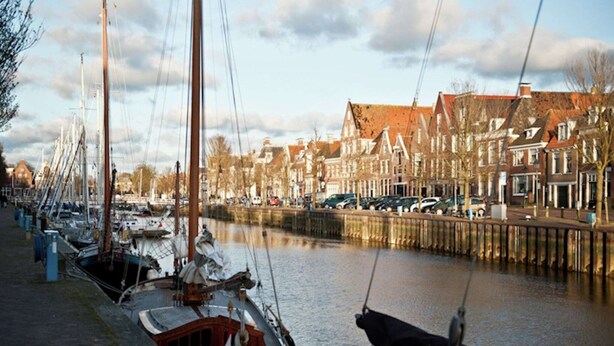 A canal with boats docked on the left, a row of traditional buildings on the right, and a clear sky above.