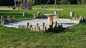A playground with a wooden ship-shaped play structure and a sandpit surrounded by wooden posts.