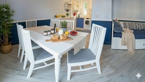 A modern kitchen with white cabinetry, a dining table with chairs, and a built-in washing machine. - Imperia City apartment (Imperia)