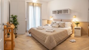 A modern bedroom with a large bed, bedside tables, a wardrobe, and a wooden bench with plants. - Imperia City apartment (Imperia)