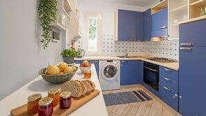 A modern kitchen with blue cabinets, a washing machine, and a wooden countertop with bread and jars. - Imperia City apartment (Imperia)