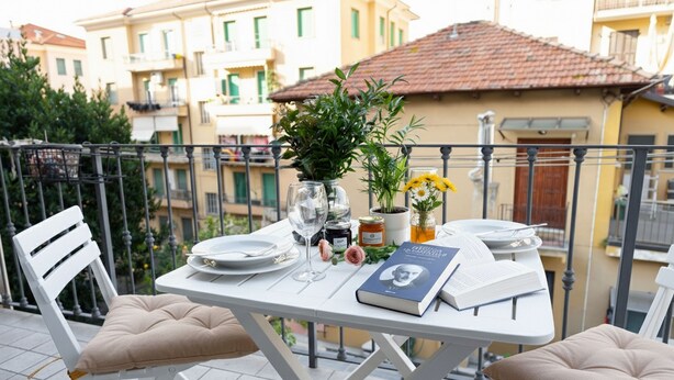 A balcony with a dining table set for two, featuring a book, a vase with flowers, and a bottle of wine. - Imperia City apartment (Imperia)