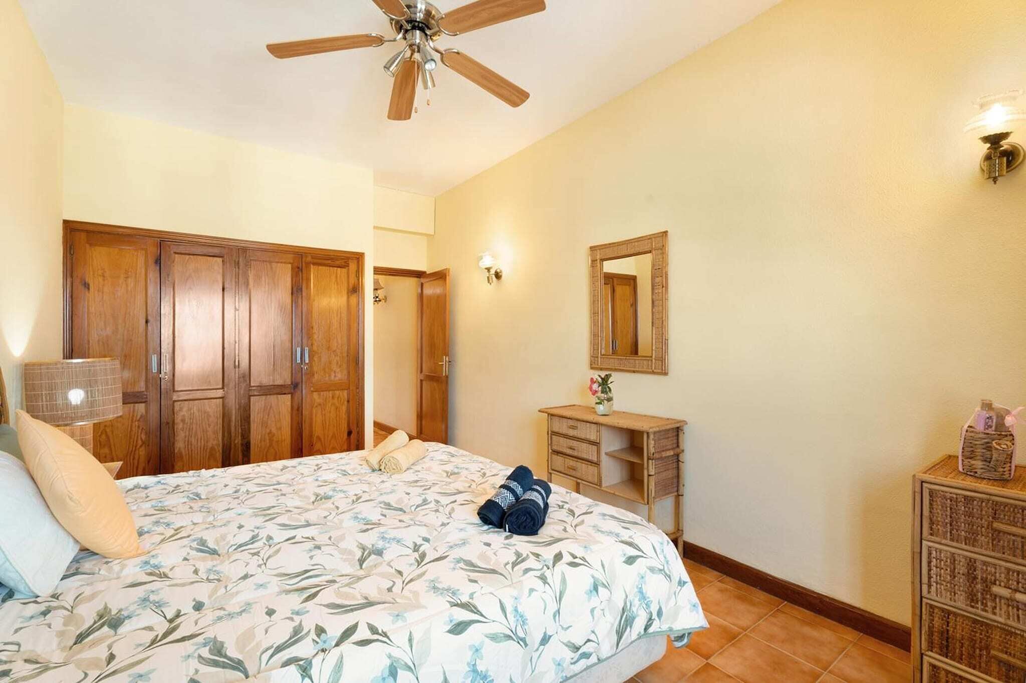 A bedroom with a bed, wooden wardrobe, desk, and a ceiling fan.