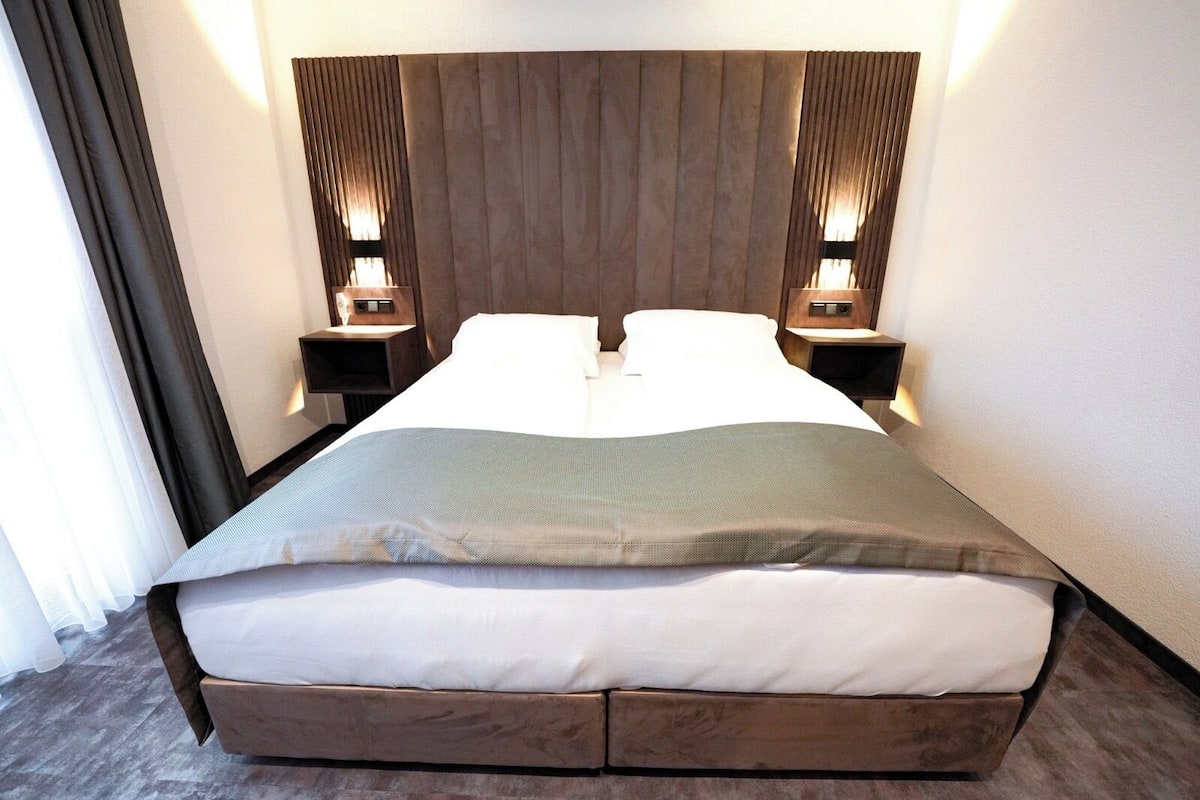 A modern hotel room with a large bed, wooden headboard, and bedside lamps.