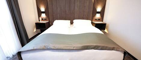 Una habitación de hotel moderna con una cama grande, cabecero de madera y lámparas de noche.
