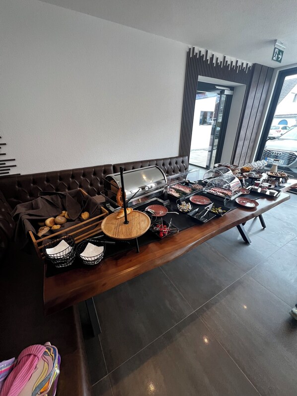 A buffet setup with a variety of food items and a seating area with a brown upholstered sofa. - JG Hotel Antoniergasse  (Memmingen)