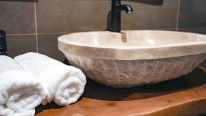 A bathroom with a stone sink, a black faucet, and two rolled white towels on a wooden countertop. - JG Hotel Antoniergasse (Memmingen)