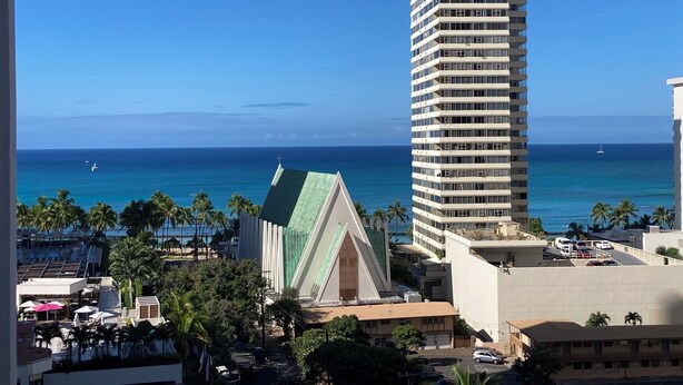 A tall hotel with a modern design, located near a beach with clear blue water and palm trees. - Waikiki Banyan 1 Bedroom with Parking! (Honolulu)