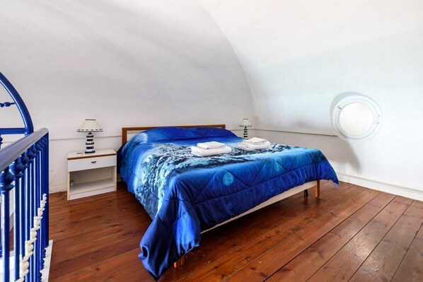A bedroom with a wooden bed, a blue bedspread, and a white nightstand with a lamp.