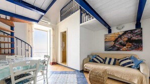 Un área de comedor con una mesa y sillas, un sofá con cojines y una escalera con barandillas azules.