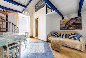 Un área de comedor con una mesa y sillas, un sofá con cojines y una escalera con barandillas azules.
