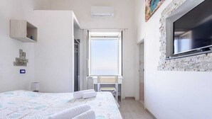 Habitación de hotel con cama, escritorio, ventana y televisor fijado a una pared de piedra.