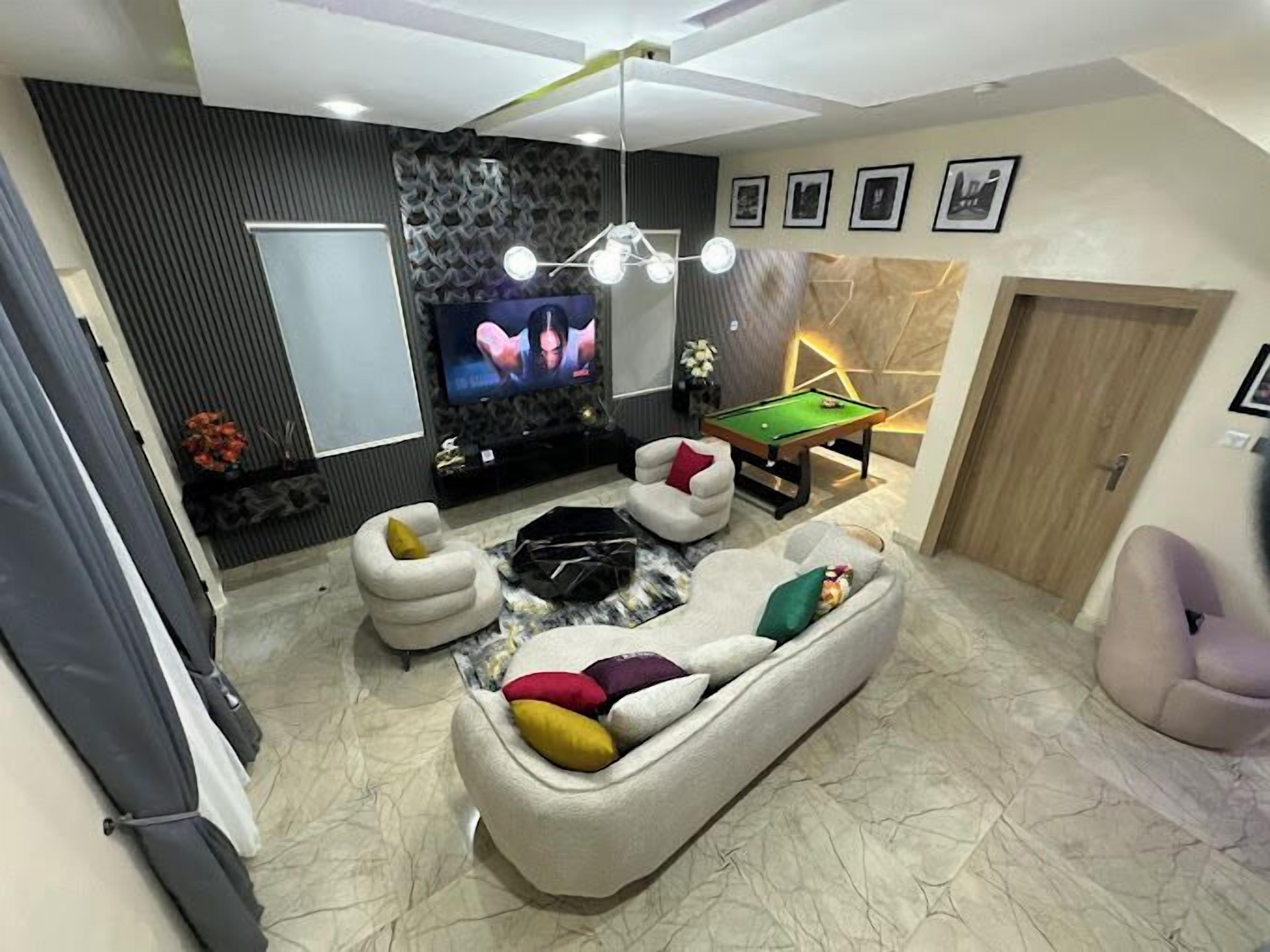 Un salon moderne avec une table de billard, un canapé agrémenté de coussins colorés, un téléviseur et un mur décoratif.