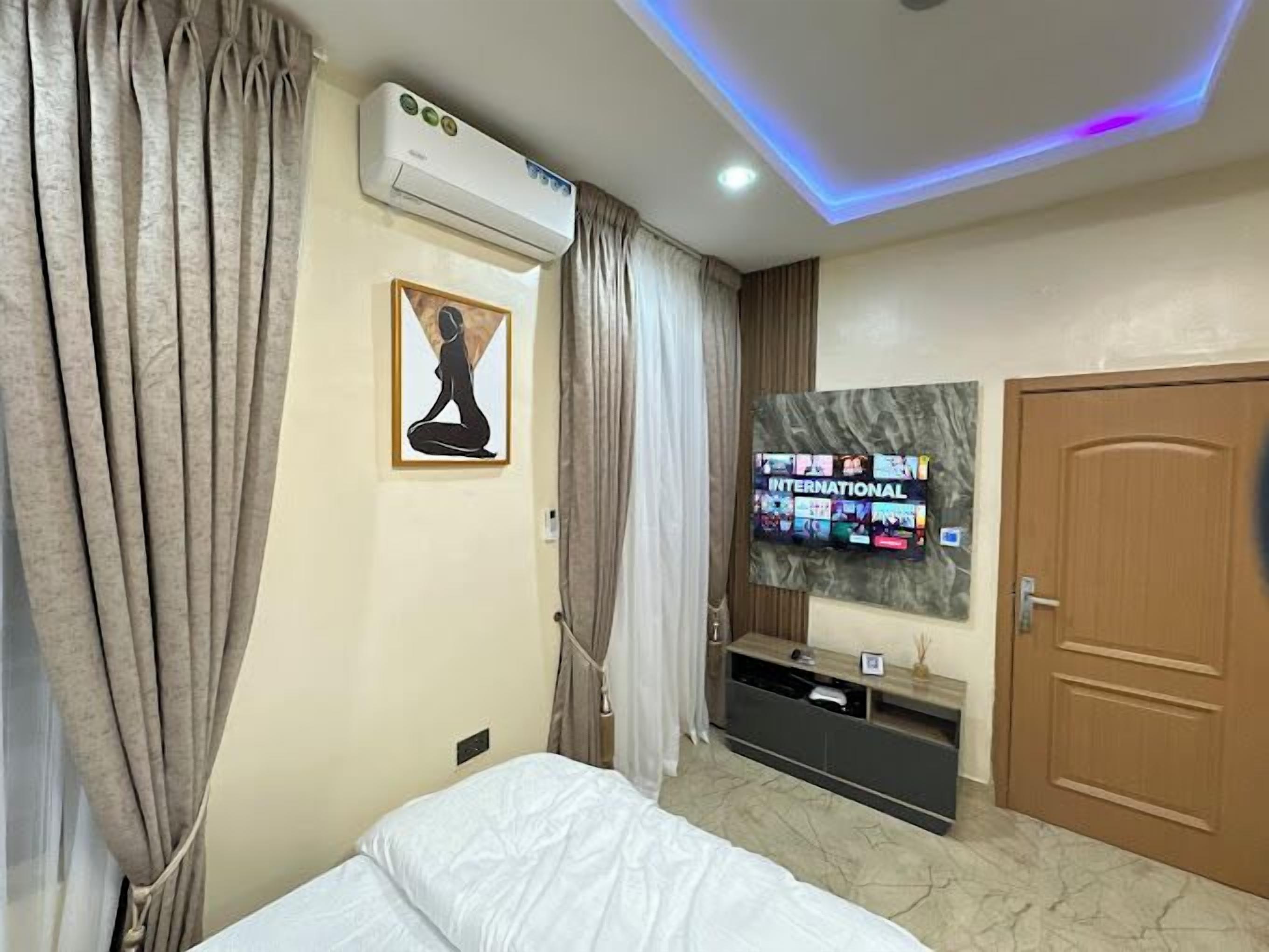 Une chambre d’hôtel avec un lit, un téléviseur fixé au mur, un appareil de climatisation et une porte en bois.