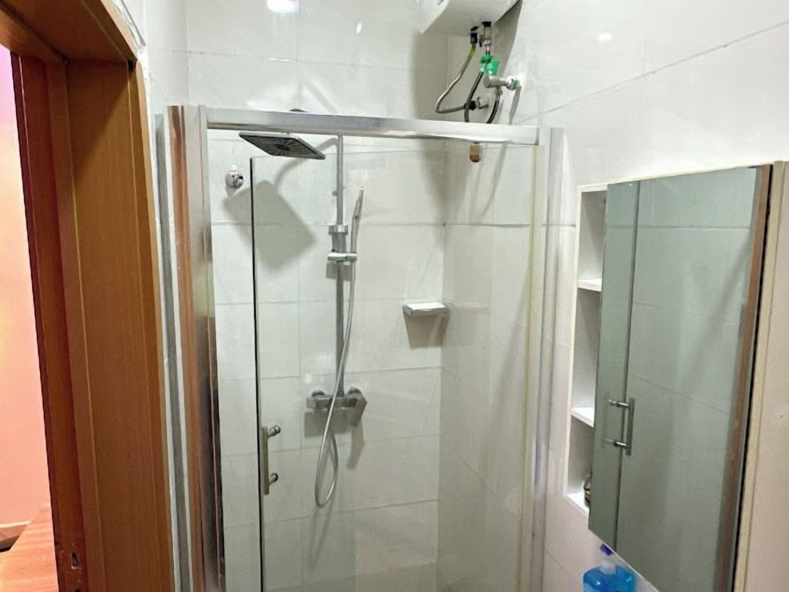 Een douchecabine met glazen wanden, een handdouche en een kraan op de muur.