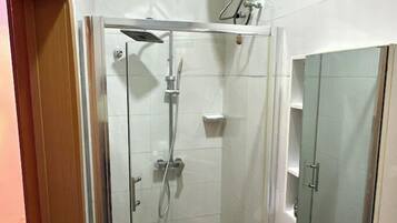 Een douchecabine met glazen wanden, een handdouche en een kraan op de muur.