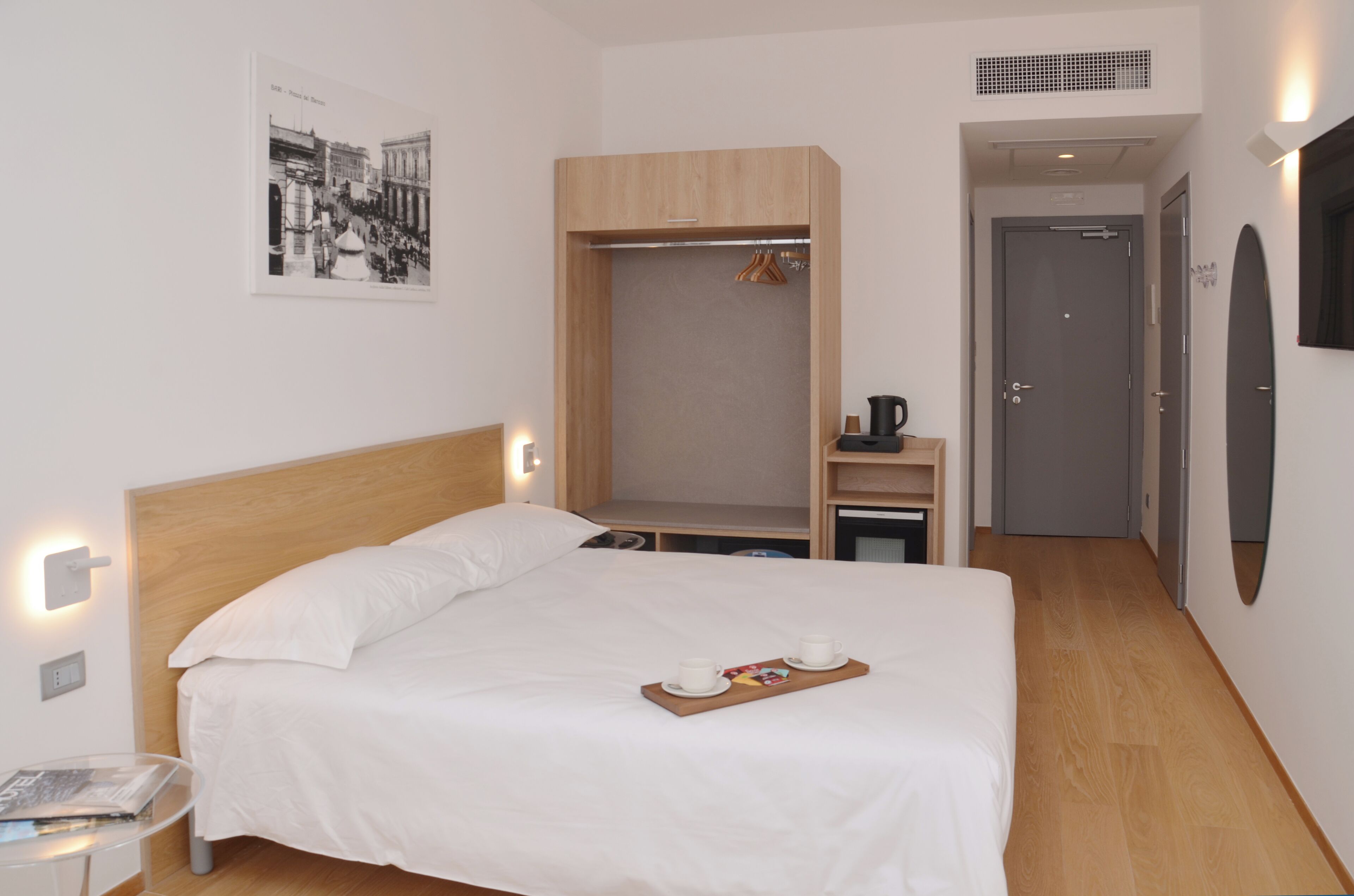 A hotel room with a bed, a bedside table, a wardrobe, a mirror, and a framed picture on the wall.