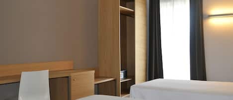 A hotel room with two beds, a desk, a chair, and a wardrobe.