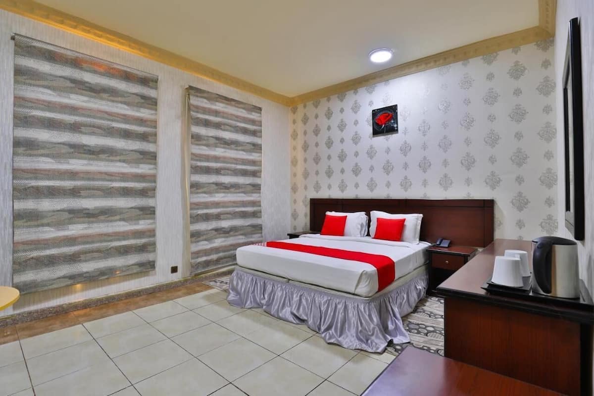 A hotel room with a bed, bedside table, and a small desk with a chair.