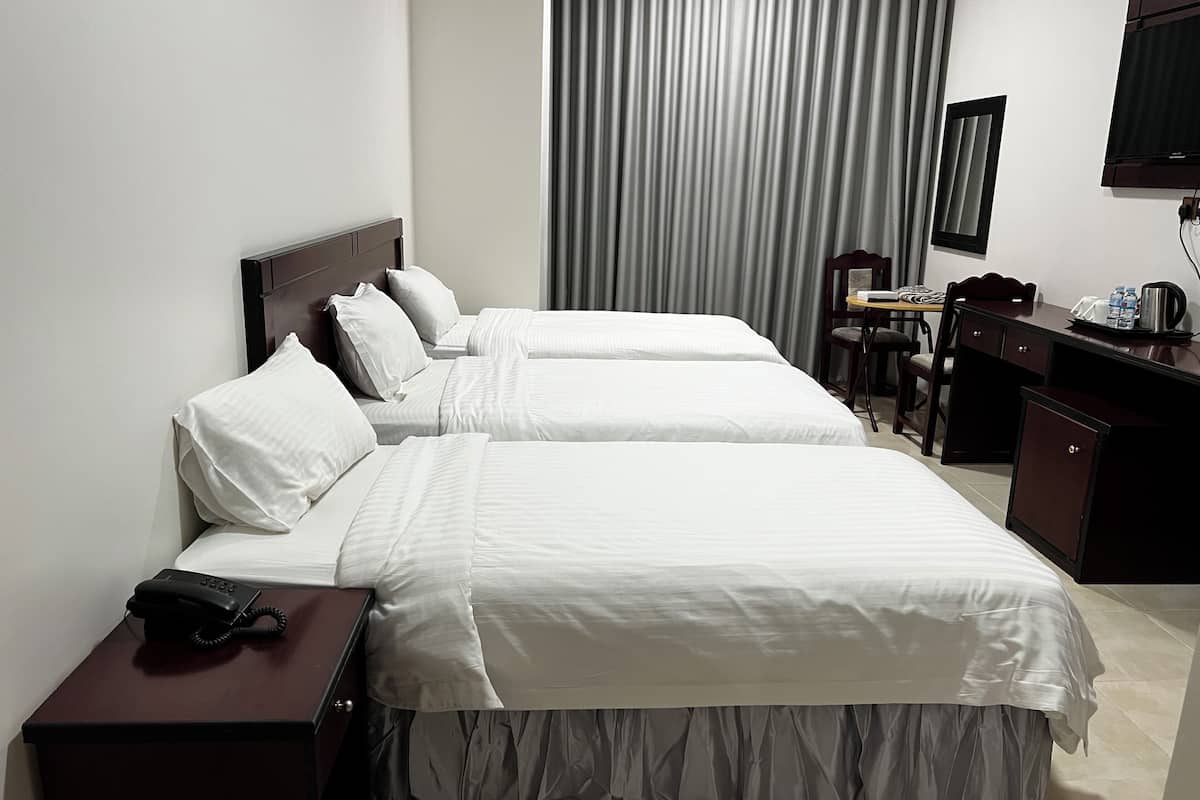A hotel room with two beds, a desk with a telephone, a chair, a small table with a chair, a television, and a window with curtains.