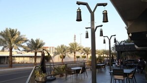 An outdoor cafe with tables and chairs, surrounded by palm trees and a street in the background. - Al Rayyan Hotel (Madinah)