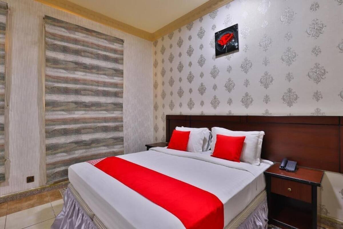A hotel room with a large bed, a wooden headboard, a nightstand with a phone, and a patterned wallpaper.
