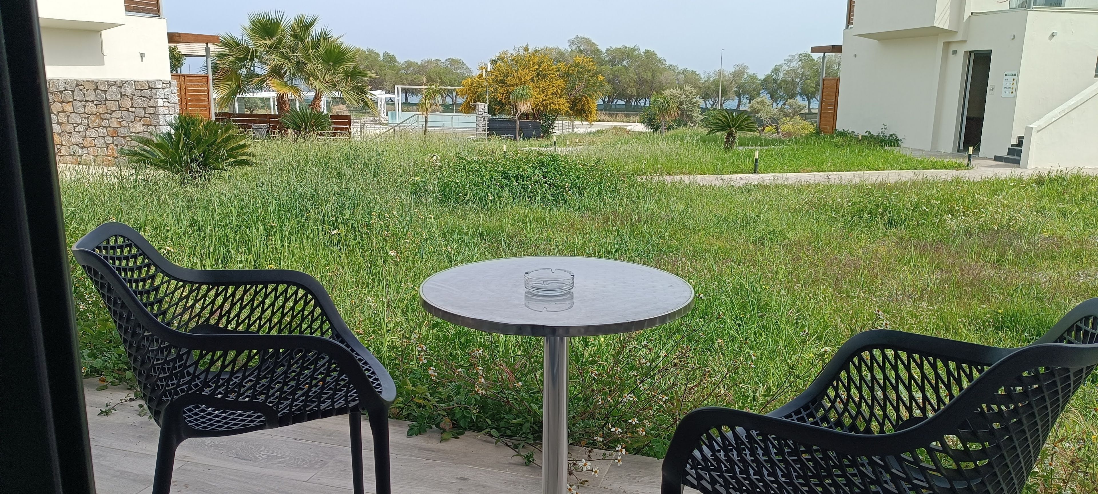 A patio area with two chairs and a table, surrounded by a grassy garden and a stone wall.